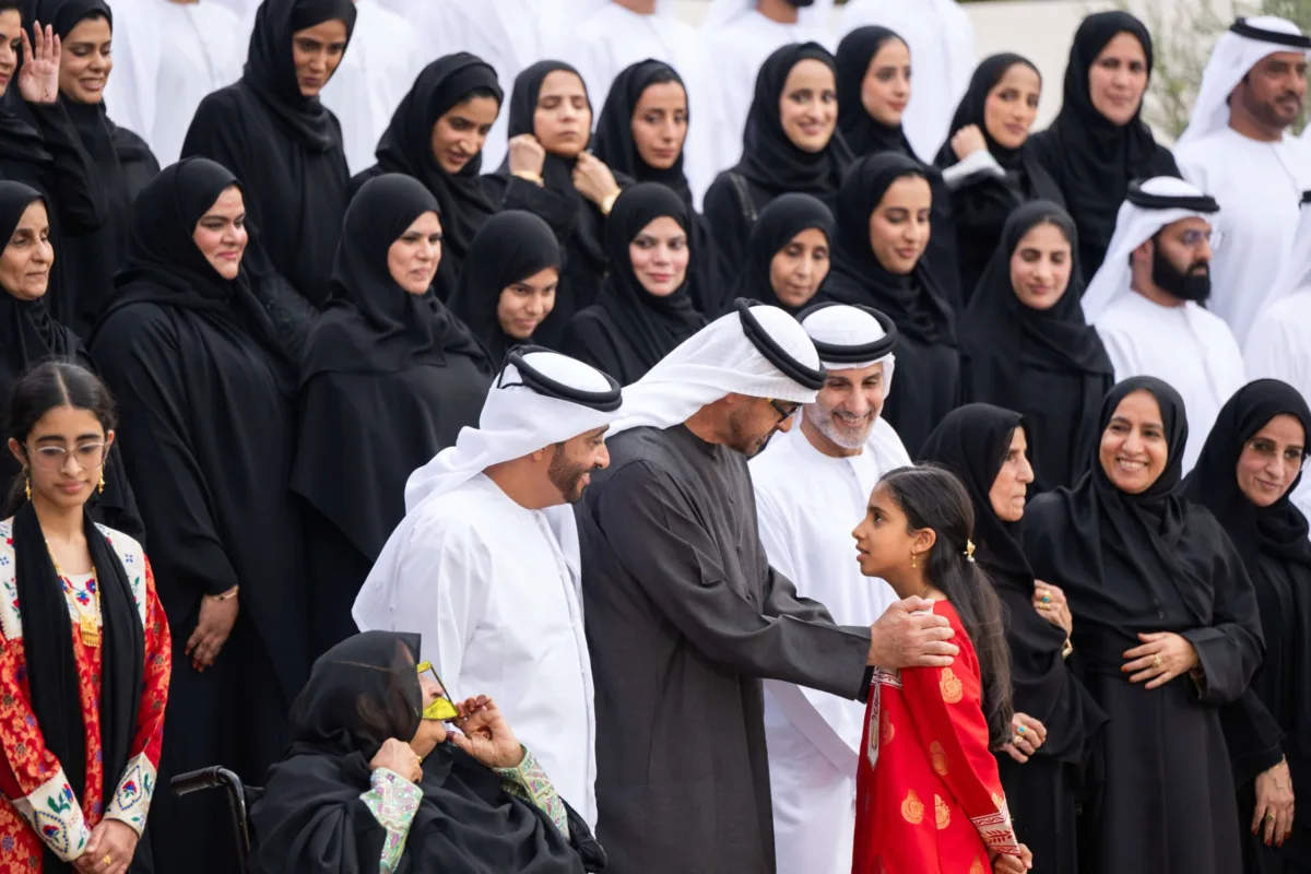صاحب السمو الشيخ محمد بن زايد آل نهيان، رئيس دولة الإمارات، يلتقي أفراد عائلة الصيري القمزي خلال مناسبة رسمية في الهواء الطلق، محاطًا بعدد كبير من الرجال والنساء والأطفال بملابسهم الوطنية، تكريمًا لدور العائلة في الإشراف على مزرعة الشيخ زايد في الخوانيج.