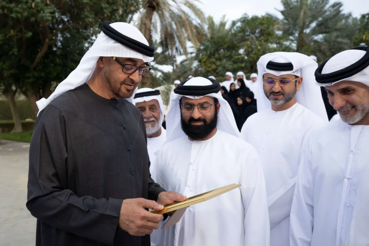 صاحب السمو الشيخ محمد بن زايد آل نهيان، رئيس دولة الإمارات، يلتقي أفراد عائلة الصيري القمزي خلال مناسبة رسمية في الهواء الطلق، محاطًا بعدد كبير من الرجال والنساء والأطفال بملابسهم الوطنية، تكريمًا لدور العائلة في الإشراف على مزرعة الشيخ زايد في الخوانيج.
