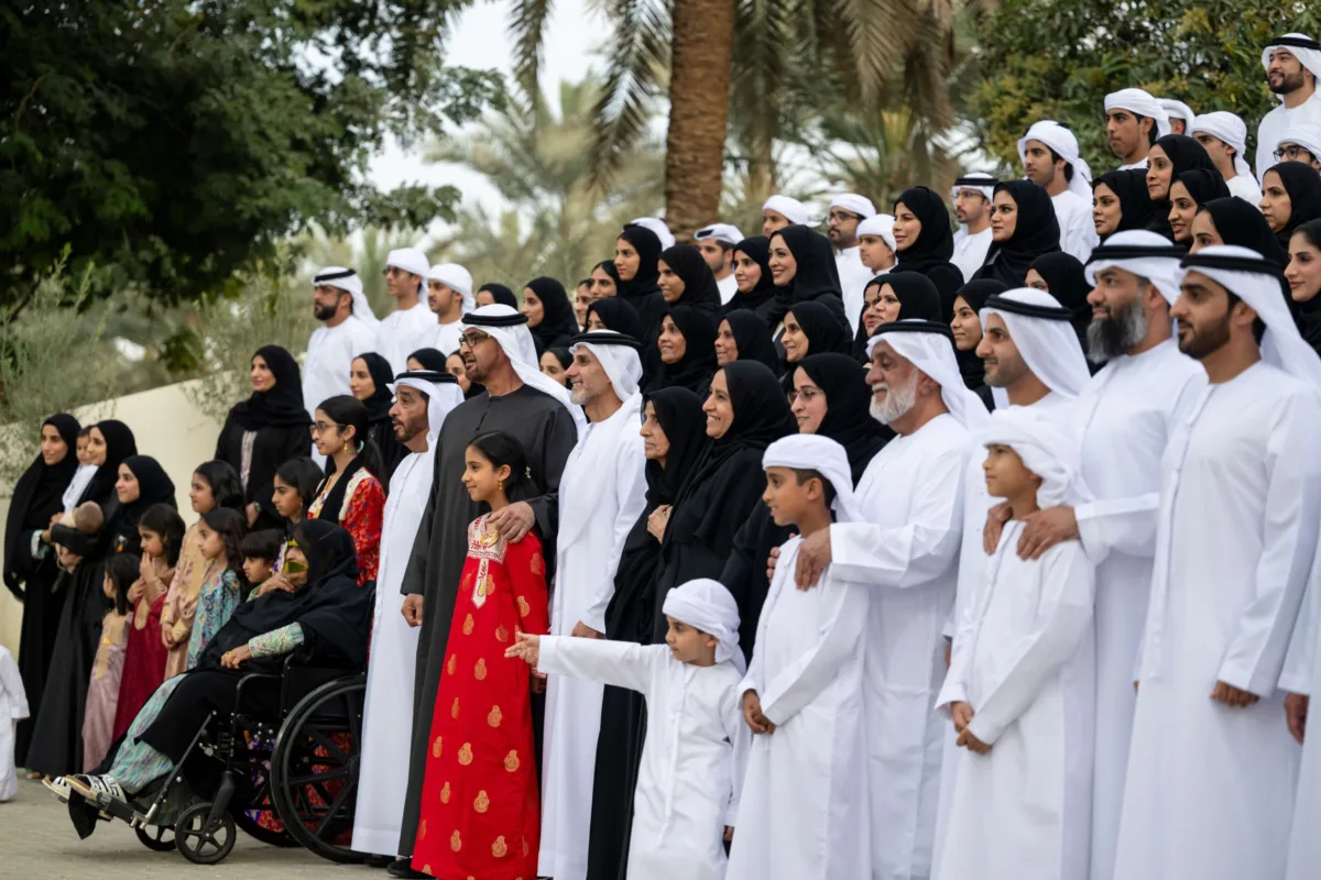 صاحب السمو الشيخ محمد بن زايد آل نهيان، رئيس دولة الإمارات، يلتقي أفراد عائلة الصيري القمزي خلال مناسبة رسمية في الهواء الطلق، محاطًا بعدد كبير من الرجال والنساء والأطفال بملابسهم الوطنية، تكريمًا لدور العائلة في الإشراف على مزرعة الشيخ زايد في الخوانيج.