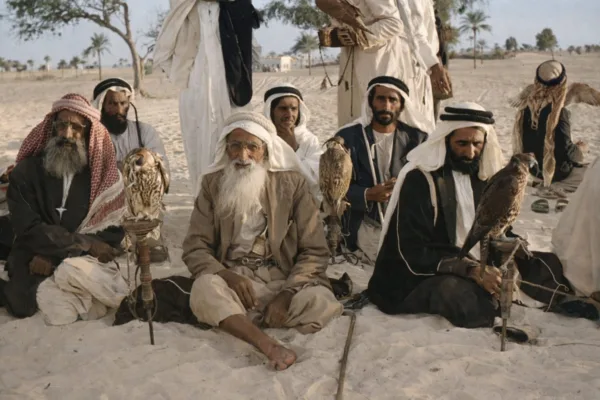 الشيخ راشد بن سعيد آل مكتوم وخليفة عبدالله مطر محمد الصيري يجلسان في الصحراء حاملين الصقور، في مشهد يوثّق الصقارة وتراث دبي الأصيل